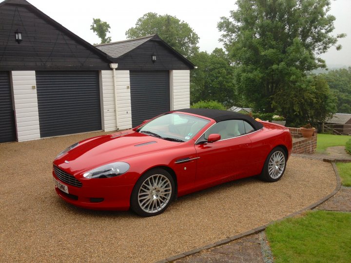 Show us your DB9  - Page 3 - Aston Martin - PistonHeads - In the image, there's a unique scene on a driveway. A red Aston Martin car is parked with the top up. The car is situated in front of a black garage with white trim, giving a stark contrast to its surroundings. 

The Aston Martin is parked on a gravel driveway, adding a touch of rustic charm to the scene. In the background, there is trees and a building, possibly a house, adding a residential feel to the image. The overall setting suggests a peaceful, upscale residential area.