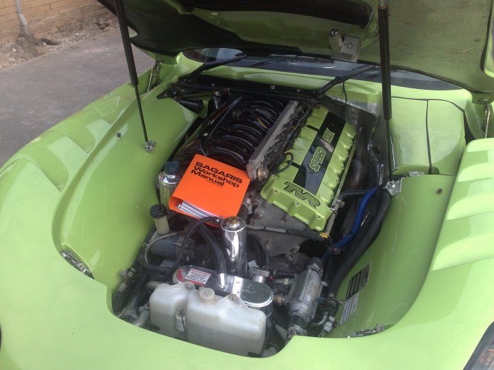 Options Colour Exterior Pistonheads - The image shows an open car's bonnet, revealing the engine and various components underneath it. Resting on the engine is a bright orange book titled "Isuzu MUX" with several pages visible, accompanied by a small red booklet. The scene is set against a dark background, enhancing the focus on the car and the books. The image is a close-up shot, providing a clear view of the engine and books. The car appears to be a compact or small-sized vehicle, given the limited view of its body.