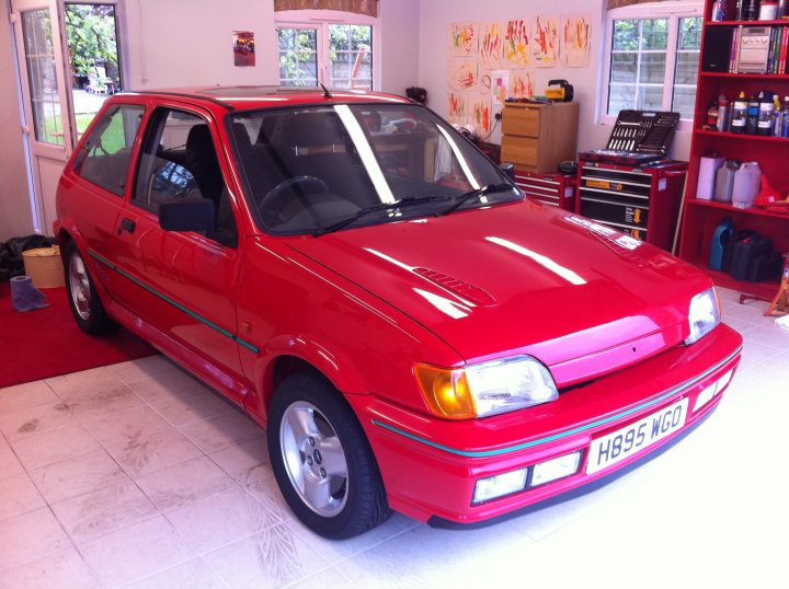 Fiesta RS Turbo Restoration - Page 13 - Ford - PistonHeads - The image features a vibrant red hatchback car parked indoors, likely within a garage or workshop. The car has a clean, shiny exterior with visible design stripes. The interior of the space looks well-organized, with neatly lined up test tubes and possibly other laboratory equipment, suggesting a scientific setting or a place used for automotive maintenance. The windows reveal a hint of external daylight and greenery, indicating that the room is part of a larger building with outdoor access.