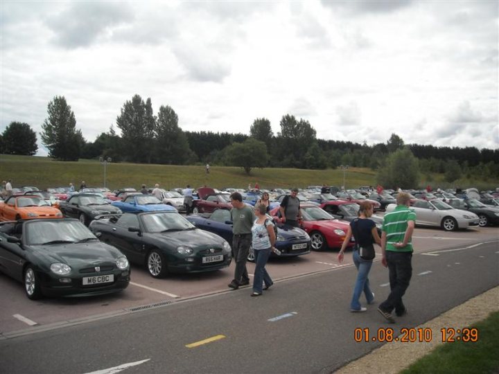 Pistonheads - The image depicts a vibrant scene of a car show. Many people have gathered, walking through the rows of parked cars. The conditions indicate it might be a slightly overcast day with a picture timed at 12:39, as per the excited date on the digital clock at the bottom.