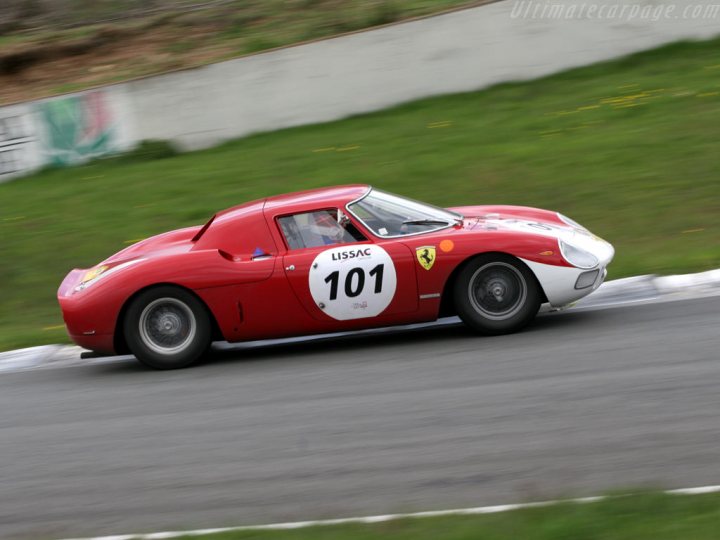 Pistonheads Ferrari Plagued Jinx Mystery - The image captures a vibrant scene on a race track. In the foreground, a Ferrari 101 sports car is in motion, its bright red color contrasting sharply with the asphalt of the track. The number 101 is prominently displayed on the side of the car, suggesting it might be participating in a race or event. The car, with its sleek design and large rear spoiler, is the main focus of the image. 

In the background, you can see a grassy bank that forms the natural boundary of the track. However, it also adds a touch of green to the otherwise predominantly red and grey image. The photo is taken from a low angle, which enhances the sense of speed and movement, as the car appears to be moving towards us. 

Overall, the image conveys a sense of motion and excitement, typical of a sports car race or event.