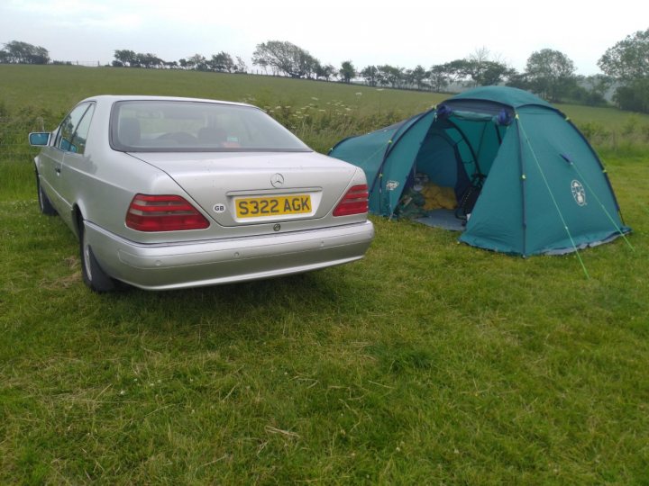 A blue car parked in a field next to a tent - Pistonheads