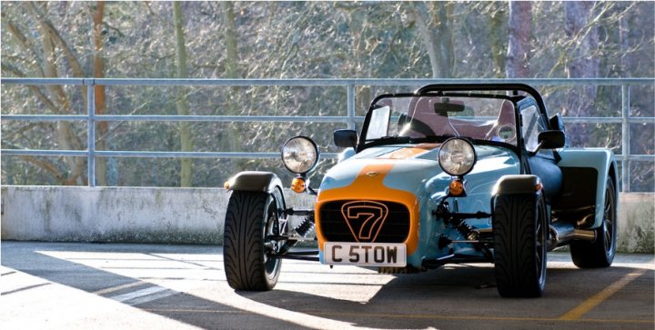 Not enough pictures on this forum - Page 13 - Caterham - PistonHeads - The image showcases a vintage, multicolored car parked in an outdoor setting. The car's detailing includes a unique color scheme with prominent shades of orange, blue, and white. It features orange and blue detailing, giving it a distinctive and eye-catching appearance. Two headlights are visible, suggesting a operating state. The overall scene is set against a backdrop of trees and a metal fence, hinting at a landscaped or outdoor region.