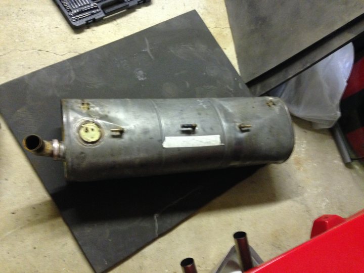 A close up of a train on a train track - Pistonheads - The image shows a cylindrical, metallic object with a silver color and a cylindrical shape, lying on a concrete surface. One end of the object is open and features a flanged connection. There is a brass plug and gasket visible on a side of the cylinder, indicating that it may have been part of a mechanical or industrial system. Torn paper tape is partially covering the flange of the object. The background suggests an industrial or repair setting.