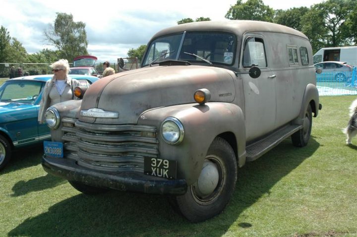 Fins and Chrome - Page 1 - North East - PistonHeads - This image features a restored gray Dodge utility truck parked in a grassy field. The truck is old, with a white license plate and its headlights turned off. Several people are standing behind the truck, and out of focus, there appears to be another vehicle and a dog in the same field. The sky is overcast, and the overall scene suggests an outdoor event or gathering.