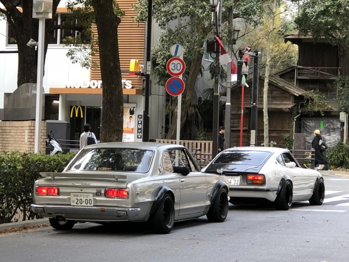 Supercars spotted, some rarities (vol 7) - Page 277 - General Gassing - PistonHeads - This image captures a vibrant street scene in Japan. Two vintage cars, a silver and black one and a white and black one, are parked along the curb, their classic designs reflecting the local culture. The street is lined with modern shops and restaurants, adding a contrast to the old-world charm of the cars. A McDonald's restaurant stands out amidst other businesses. Pedestrians can be seen walking on the sidewalk, contributing to the lively atmosphere of the city. The image also contains some text that reads "WASH POWER", possibly indicating a local business or a public service announcement.