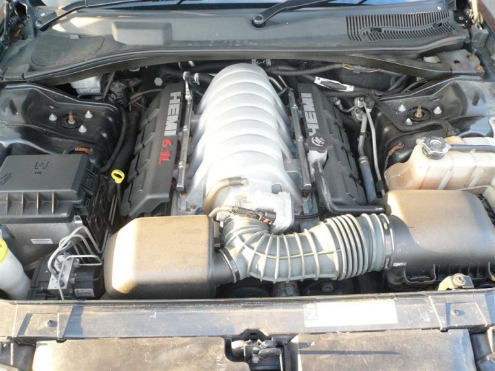 Pistonheads - This image shows an open hood of a car, revealing the engine components. The engine is large, with visible EXP ti peaks. There is a red Hemi label on the engine, suggesting it is a Hemi engine. Aside from the engine, there are various cables and wires connecting different parts of the vehicle. The vehicle appears to be quite large, perhaps a large SUV or truck. The hood is propped open, possibly for maintenance or inspection.