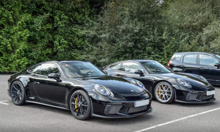 Are there really 47 GT3 tourings in the UK (C16) - Page 26 - 911/Carrera GT - PistonHeads UK - The image showcases a collection of luxury sports cars parked in an outdoor lot. There are two black sports cars, one with yellow accents and the other with gold accents. Adjacent to these cars is a silver sports car with black rims. The cars have custom modifications like large wheels and low suspension, which give them a sporty and aggressive look. They are parked on what appears to be an asphalt surface in front of some trees and a building. The setting suggests that this might be a special event or show dedicated to high-performance vehicles.