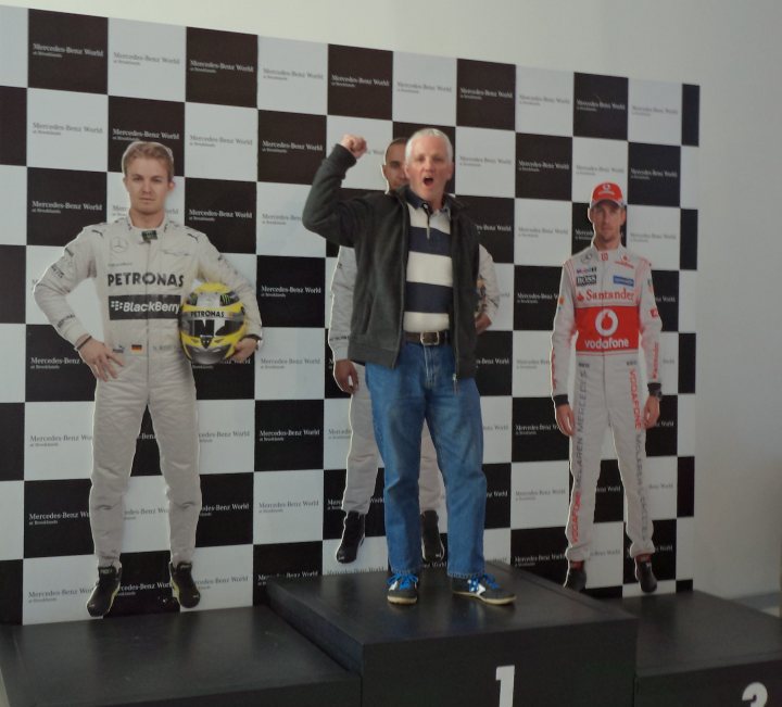 A group of young men standing next to each other - Pistonheads - The image features a man posing proudly on a podium. He's celebrated with a sprint car racing backdrop, comprised of cut-out cardboard stands of racing figures that include real drivers. The driver cut-outs are integrated with the race track design, creating a fun, unreal photoshop effect. The man is dressed casually, in jeans and a striped shirt, which contrasts with the hyperreality of the racing backdrop. His posture suggests he's enjoying the moment, perhaps pretending to race himself.