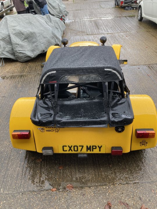 Pistonheads - The image shows a bright yellow vehicle, possibly a classic car or convertible sports car, parked outdoors. The vehicle appears to have an open-top design, suggesting it might be used for recreational purposes or convertible use in different weather conditions. It is parked on what looks like a street, and there's a wet surface around the car, indicating recent rainfall. In the background, there are other vehicles and some personal belongings scattered around, indicating that the area might have been recently used by people who were outdoors. The image has a candid quality to it, suggesting it was taken in an informal setting rather than a formal photoshoot.