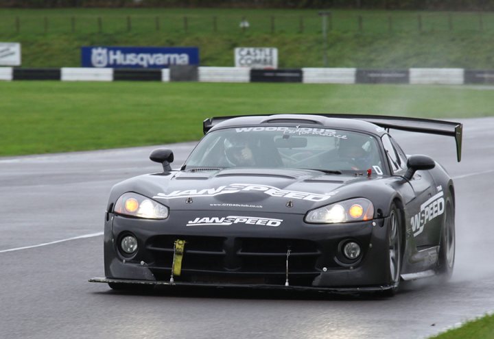 Pistonheads - The image captures a dynamic scene on a wet road. A black sports car with a wing on the rear, bearing the number 18, is racing down the track. A person is seated in the driver's seat, their eyes visible through the windshield, indicating their active engagement in driving. The car's license plate and wing read "JANSPEED," suggesting it's a race vehicle. The background reveals a grassy landscape with a race track, indicating that this is likely a racing event. The wet road reflects the car, adding to the intensity of the scene. The image conveys a high-speed motion, as the car appears to be accelerating.