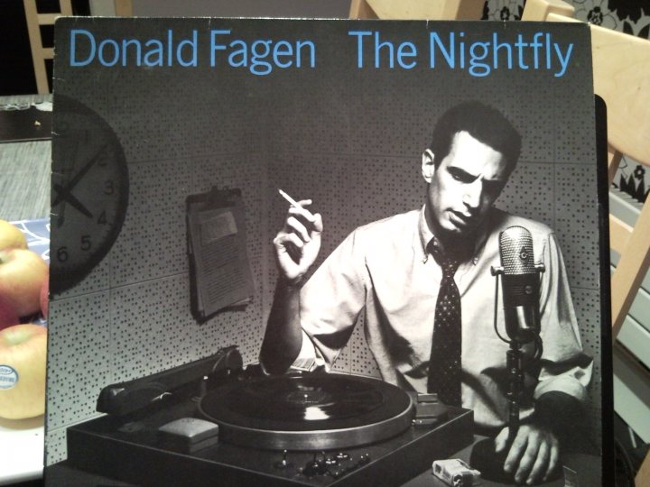 Pistonheads Vinyl Fine - The image features an album cover for "Donald Fagen, The Nightfly." The album cover has a vintage, black and white look and prominently features Donald Fagen smoking a cigarette. Fagen is seated behind a record player, and the background indicates he is in a recording studio. The album cover suggests a nostalgic, possibly retro theme, aligning with Fagen's jazz-influenced music.