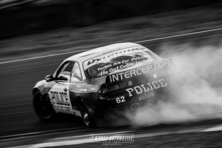 It can't really be mistaken for a British police car - Page 1 - General Gassing - PistonHeads - This image captures a dynamic scene on a race track. Speeding cars, with one particularly pronounced in the foreground, are seen driving at high speeds. This car, emitting a cloud of smoke as it races, is a police car labeled with the number 62. The car's motion, conveyed through the blur of its tires and the smoke trail, seems to be evading or pursuing another vehicle, as indicated by the text on the police car that reads: "Pu$$ are challenged Maybe they don't want to lose again to a police Intercepter. It's an INSTINCT. TRAFFIC, SAFETY What hold them back, maybe fear". The atmosphere of the image suggests intensity and high-stakes chases, illustrated by the use of black and white photography.