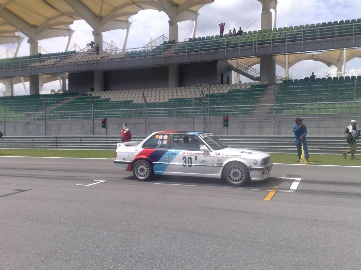 Sepang Afos Pistonheads - In the heart of a bustling city stadium, a car race is in full swing. Two cars, swift and powerful, are battling for the lead on the track. The driver in the blue and red car is inching closer to the white and black car, the number 30 emblazoned on it. Seated in the passenger's seat, a balloon any racer would envy is in the blue and red car. In the background, spectators fill the stands, their eyes glued to the thrilling duel on the track. The atmosphere is electric, the air vibrant with anticipation. This is more than a race; it's a dance between velocity and strategy, a spectacle of speed and skill.