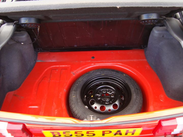 Won Lottery Feel Ive Pistonheads - The image reveals the underside of a car, focusing on the rear. The area is painted a vibrant red, with black elements visible beneath the painted finish. A spare tire neatly tucked away in the back storage area. A license plate is affixed, reading "B555 Pah" and consists of yellow letters on a red background. The luggage rack present above the rear storage area.