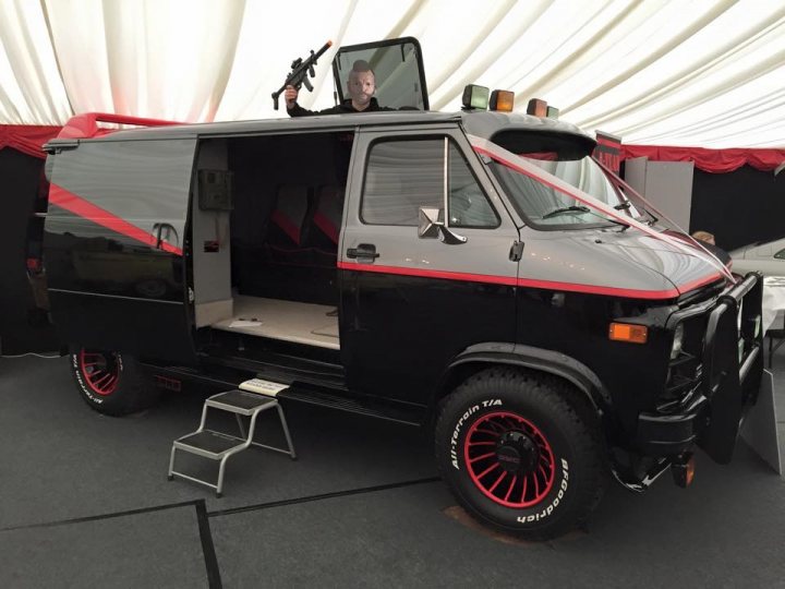 Prom transport plea... 26th June 2015 - Page 1 - East Anglia - PistonHeads - The image features a black and red van parked under a tent. The vehicle, with its window open and a person inside, exudes a sense of adventure. A distinctive red stripe adorns the van, adding to its bold look. The tent underneath, with its red draping, contrasts nicely, enhancing the overall ambiance of the scene.