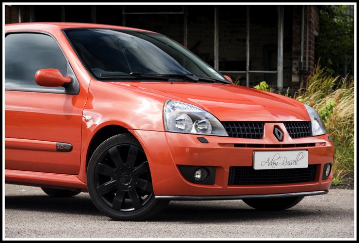 Introduce Thought Pistonheads - The image showcases a vibrant red hatchback car parked outdoors. The vehicle is positioned perpendicular to the visible part of the frame, with its side profile clearly visible, exposing its door, window, and the car's unique design. The car's license plate displays the purple text "LR-844," adding a touch of personalization to the vehicle. In the background, you can spot the exclamation of a tree, partially obscured by the car, and part of a building, suggesting the car is parked in an urban or suburban setting. The overall image exudes a modern and colorful aesthetic.