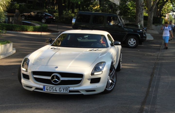 SLS & celebrities - Page 1 - Mercedes - PistonHeads - This image depicts a city street scene with a white, two-door Mercedes car parked near the sidewalk. The car is facing towards the right side of the image, and it has its headlights on, suggesting it might be a sunny day with the need for light near or before the vehicle.

Across the street, there's a person walking by, giving a sense of life and movement in the scene. On the left side of the image, there's another car, hinting at the multi-lane road leading up to the Mercedes.

In the background, there are trees providing a touch of greenery to the urban environment. The sky is partly cloudy, adding a dynamic element to the overall setting.

Overall, the image captures a typical day in a city, with a focus on a Mercedes car parked on the side of the road.