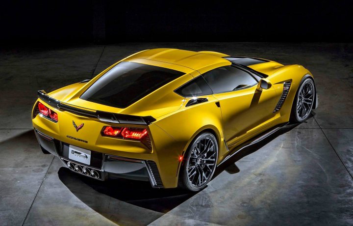 C7 Z06  - Page 1 - Corvettes - PistonHeads - The image showcases a striking yellow Corvette C8.R sports car. Its sleek design includes a low and wide stance, with sporty features like a large rear wing and a prominent front splitter. Carbon fiber accents are visible, including a one-piece front hood with large vents and a hood louvers for heat release. The car rests on unique wheel designs typical of the Corvette, and the headlights are a bright, captivating light. The setting appears to be a darkened indoor space, focused solely on the car, highlighting its details and the car's glimmering paint.