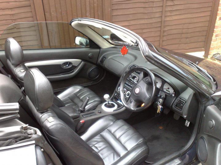 Pistonheads - The image features an interior view of a car with the trunk open. The car appears to be a small, two-door sedan with a leather interior. Several items are visible inside the car, and on the gear shift, there is a small, red ornament. The dashboard and steering wheel are visible, and the gear controls are also part of the image. The exterior of the car is not fully visible, but it seems to be a sunny day.