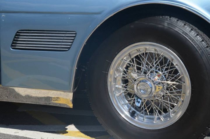 Refurbishment of my Maserati Mexico - Page 17 - Classic Cars and Yesterday's Heroes - PistonHeads - The image depicts a close-up view of a silver car's wheel. The wheel's spokes are finely detailed and shiny, and the overall condition of the tire suggests it's well-maintained. The car is positioned on a road or parking area, and the ground visible in the image indicates asphalt or concrete. The focus of the image is the wheel, with the rest of the car and its surroundings out of focus.