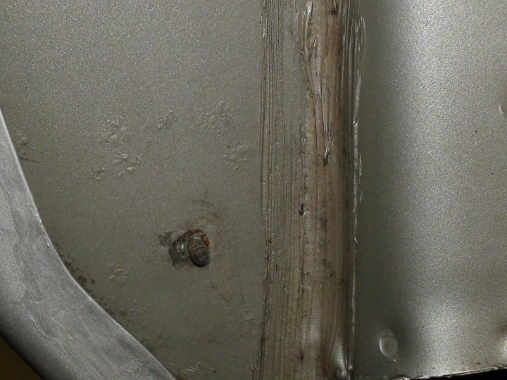 Rust Problems and Getting the Manufacturer to fix it - Page 1 - General Gassing - PistonHeads - The image shows a close-up of a metallic object with a black surface rendered in shades of gray and brown. There are marks and scratches on the surface suggesting some level of usage or wear. A single small screw with a rusty appearance is visible, partially embedded in the object. The metallic object's overall condition might hint at its age or exposure to the elements.