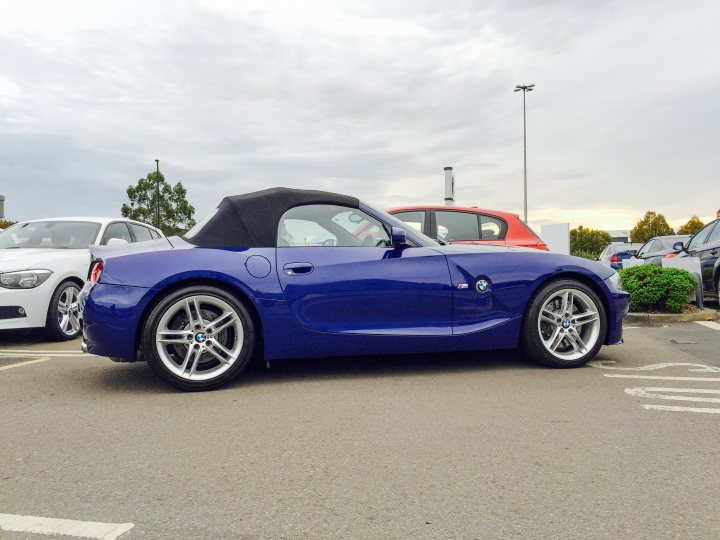 Show us your SIDE! - Page 25 - Readers' Cars - PistonHeads - This image captures a scene in a parking lot with several cars parked. The main focus is a vibrant blue BMW convertible, its top down, parked facing towards the right side of the picture. The vehicle is sleek and modern, giving off an aura of luxury. Behind the BMW, there are other cars and various parking equipment, including parking meters and street lamps. The sky provides an overcast backdrop to the scene, hinting at the possibility of rain or an impertinent sky.