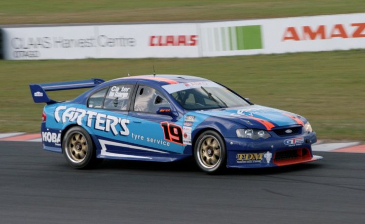 A car that is sitting in the street - Pistonheads - The image features a vibrant sports car in the midst of a race track, captured mid-veer on a sharp turn. The car is predominantly blue, with orange and white paneling, prominently showcasing the sponsor and racing number. The track itself appears to be in motion, with a sense of speed and excitement permeating the scene. The backdrop is a blur of other racing vehicles and trackside structures, emphasizing the fast-paced, adrenaline-fueled nature of the competition.