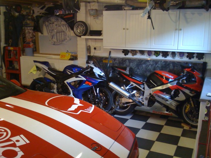 Just sorted my garage - Page 1 - Vipers - PistonHeads - The image features a garage or workshop setting, specifically focusing on a collection of motorcycles. There are at least three distinctive motorcycles parked in the room, with two prominently positioned alongside a red race car or modified sports car. The motorcycles exhibit a variety of designs and colors, while the red car stands out with its vivid hue and unique, possibly custom, design elements.

The room itself is utilitarian, with a black tile floor that reflects the ambient light, emphasizing the clean surfaces. On the left side of the image, there is a whiteboard or wooden panel adorned with various fixings or personal items, indicative of a working space.

Overall, the scene is a blend of well-kept machinery, with the precise location of each item suggesting a working or recreational environment where owners or enthusiasts may spend time on maintenance, modification, or simply enjoying their vehicles.