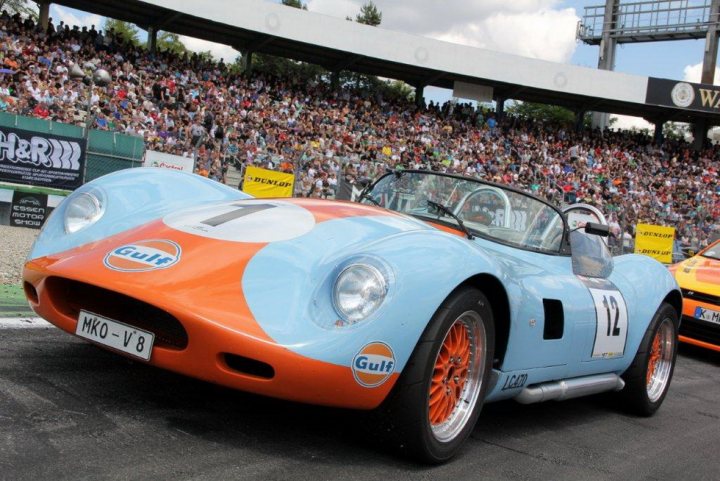 A car that is sitting in the street - Pistonheads - The image captures an exciting moment in a car race taking place in a large outdoor stadium. A blue and orange sports car, bearing the number twelve and the word "GUIL" prominently displayed on its side, is the main focus of the scene. The car is in motion, seemingly in the middle of a race. The audience in the stands forms a blurred backdrop, their attention riveted on the race. In the distance, other cars can be seen, further highlighting the dynamic nature of the event. The contrast between the vibrant colors of the cars and the mostly green landscape, punctuated by the clear blue sky, adds a sense of vibrancy to the scene. The image exudes the adrenaline-fueled excitement and competitive spirit of a high-speed sporting event.