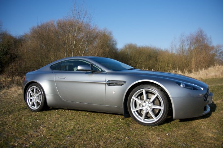 Friend Pistonheads Goodbye - The image displays a silver sports car parked on a grass surface. A few trees and bare branches are visible in the background, suggesting a park or woodland setting. The car appears stationary, and its sleek design and black tires contrast with the green grass and blue sky. The lighting suggests the photo was taken during the day under clear skies.