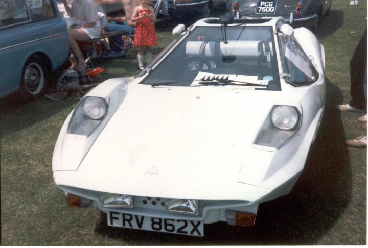 RE: Adams Probe owner calls for help - Page 2 - Classic Cars and Yesterday's Heroes - PistonHeads - The image shows a vintage white sports car parked on a grassy area. In the background, there is a person standing and watching the car, and there is also a child standing near the car. Other cars are visible in the distance. The car has distinct headlights and is an interesting piece of history.