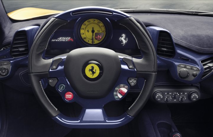 speciale spider is here  - Page 1 - Ferrari V8 - PistonHeads - This image features the interior of a vehicle, focusing on the steering wheel and instrument cluster. The steering wheel is black with a yellow Ferrari symbol at the center, featuring a silver prancing horse emblem. Behind the steering wheel, the dashboard has a visible instrument cluster with a yellow speedometer and a black tachometer behind it. The controls and buttons for various features and functions are typical of luxury and performance vehicles.