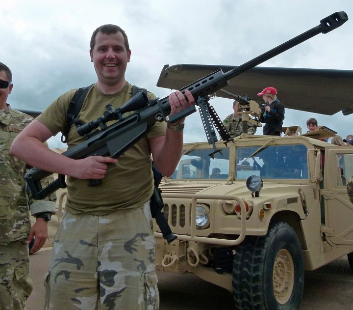 A man in a military uniform is holding a skateboard - Pistonheads - The image captures a moment of camaraderie and preparation. A man, casually dressed in a green shirt and khaki pants, confidently holds a rifle, ready for action. His laughter suggests a light-hearted sense of adventure.

In the background, an army humvee is parked, indicative of the military setting. A companion, identifiable by his military fatigues, accompanies the man, adding to the narrative of readiness and purpose. 

Above them, the sky is cloudy, the overcast day perhaps hinting at an upcoming mission. The scene is a blend of everyday life and military preparedness.