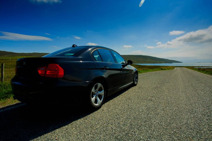 BMW 320d E90 series, which iteration is best/most reliable? - Page 2 - General Gassing - PistonHeads - The image captures a moment of solitude on a road with a picturesque view of a vast landscape. A black car is parked on the side of a road, under a clear blue sky speckled with clouds. The car is positioned on the roadside, its sleek silhouette contrasting with the natural surroundings. 

In the background, a serene body of water can be seen, adding a tranquil touch to the scene. The landscape is predominantly green and brown, suggesting an outdoor setting. Beyond this, misty mountains rise against the horizon, their peaks disappearing into the sky. 

The image conveys a sense of peace and tranquility, with the parked car and the expansive natural scenery taking center stage. It's a snapshot of a calm journey, with the open road and the beauty of nature playing integral parts in the composition.