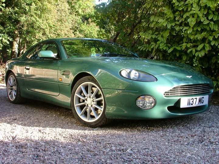 Your DB7 pictures. - Page 1 - Aston Martin - PistonHeads - The image shows a vibrant green Aston Martin car parked on a gravel surface. The car is sleek and shiny, with a shiny black top. The gravel appears dry and is scattered with small stones. The setting suggests a rural or semi-rural location, as indicated by the greenery and trees in the background. The Aston Martin is positioned at a slight angle to the camera, showcasing its front end and full view of the side. The car has a distinctive design with a large, oval-shaped grille that is characteristic of the Aston Martin brand. The year plate on the car reads "2005". Overall, the image captures the elegance and style of the Aston Martin, against a natural backdrop.