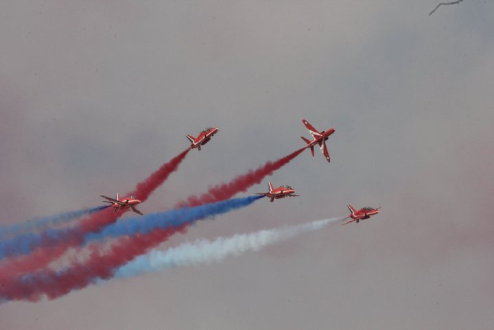 A group of planes flying in the sky - Pistonheads - The image captures a dynamic scene of a six-plane formation in mid-air against a backdrop of a hazy gray sky. Each plane is carrying out a daring maneuver, leaving behind bright trails as they soar. The planes appear to be performing a stunt, demonstrating precision and coordination in their formation. The red and blue smoke trails suggest high-speed motion and a sense of excitement and energy.