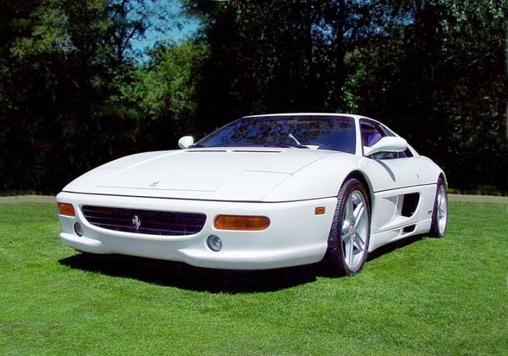 Pistonheads Nose Change Respray Colour Ferrari Complete Tail - The image shows a white convertible car parked on a grassy surface, with trees visible in the background under what appears to be a clear sky. The car has a distinctive design, typically found on sports cars, with a rear spoiler, a sleek design, and large rear wheels. It's parked with its hood facing forward. The setting seems serene and could possibly be in a country or residential area due to the tree-lined background and the lush green grass.