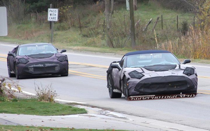 A car that is driving down the road - Pistonheads - The image shows a road with two cars visible in the scene. Both cars appear to be modified with black or gray body wraps that might mask their original colors or designs. The car on the left has a partial, longish black cover over it, while the one on the right has a similar covering primarily over the hood area. They both seem to be traveling on a highway or road with a speed limit sign nearby. There is a section of the pavement that appears to be being repaired, as indicated by the presence of pothole signs and the presence of a bnw sign, which often stands for 'best not worn,' but is here in a metaphorical sense for a roadwork area.