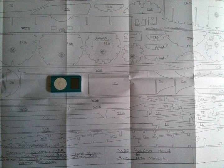 Bomber Kemble Vulcan Pistonheads - This image displays a piece of paper with hand-drawn sketches and lines of text. The sketches are detailed, showcasing plans that include geometric shapes, lines, and areas labeled with numbers. A small square section, potentially containing microchips or components, is placed at the center top of the paper. The overall content of the drawing and the presence of the component hint at a technical or engineering context. The writing appears to be related to the drawings, possibly providing information about the schematic or layout depicted in the sketches.