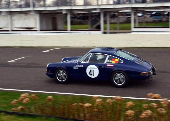 Robert Barrie Track day 24th Feb - photos - Page 1 - Goodwood Events - PistonHeads - The image depicts a vintage racing Porsche wearing number #41, tearing down a winding road or race track. The car, painted in a vibrant shade of blue, is photographed from a perspective slightly behind and to the left. The body of the vehicle is adorned with numerous decals and stickers, signifying various sponsors. The setting includes a hint of the outdoor environment with greenery and flowers. The action captured suggests speed and motion, adding a dynamic feeling to the scene.