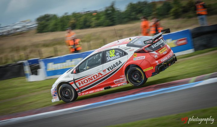 BTCC - Knockhill - Page 1 - Scotland - PistonHeads - The image captures a thrilling moment on a race track. A red and white race car, emblazoned with the Honda logos, is in the midst of a dynamic turn. The driver, clad in a matching racing suit, is leaning into the curve, demonstrating the car's agility. In the background, several individuals, possibly crew members or officials, are visible on the sidelines, adding to the intensity of the scene.