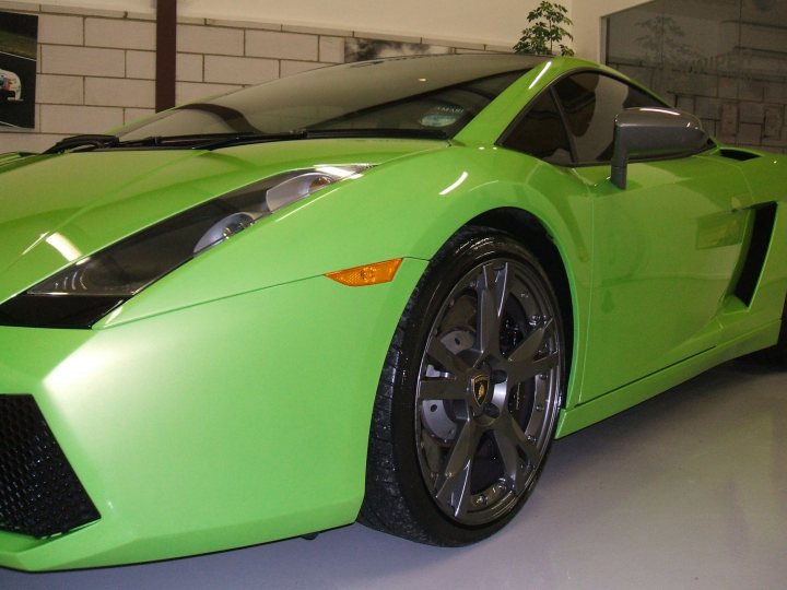 my detailed mistress pics - VI gallardo - Page 1 - Gallardo/Huracan - PistonHeads - The image features a green sports car with a sleek design, prominently displayed indoors. The car is shining, suggesting it is well-maintained or possibly freshly polished. Its design includes aerodynamic body curves, large side air vents, and distinctive, thin headlights. The car's wheels have a multi-spoke design, hinting at high-performance capabilities, and it appears to be a Lamborghini model. The background of the image is minimal, with a potted plant visible in the back, providing a contrasting element to the high-end vehicle.