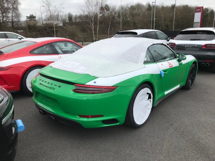 991 GTS Must haves - Page 176 - 911/Carrera GT - PistonHeads - The image showcases a bright green Porsche Cayman parked alongside other cars in a single or double level parking facility. The distinctive green color of the car is accentuated by a white vinyl car cover, which suggests that the car might be either new or that the owner prefers to protect it from the elements or discoloration. The car appears to be in pristine condition, with a gleaming finish that reflects the overhead lighting. The setting suggests a day with overcast weather conditions, as evidenced by the diffused light illuminating the car and its surroundings.