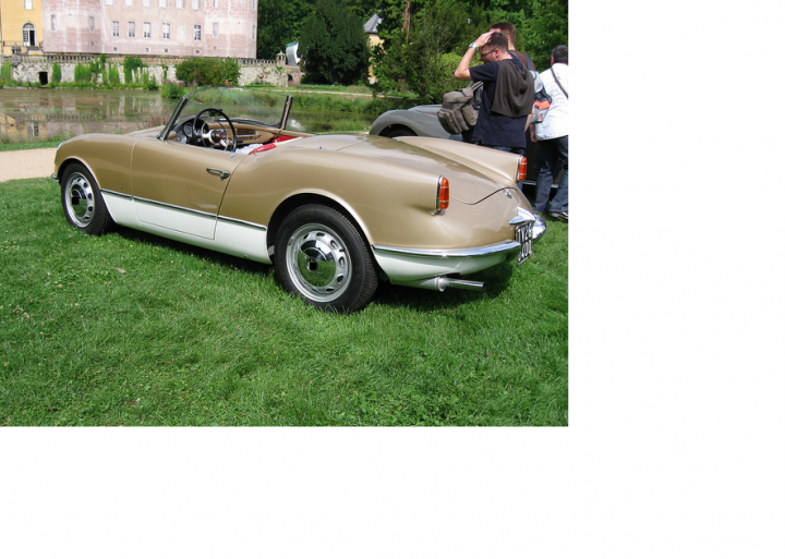 Guess the car! - Page 116 - General Gassing - PistonHeads - The image features a light-colored convertible classic sports car on a grassy area, which appears to be a garden or park. The car is old and has no top, allowing a clear view of its interior. The bodywork shows some signs of age, and the car is parked facing to the right. Behind the vehicle, there is a serene backdrop of a water body with greenery, partially obscured by tress. In the distance, there is a building with a traditional European design, suggesting that the car might be in a historical or cultural setting. The overall perspective of the photo appears to have been captured from someone standing partially behind the vehicle, as if the photographer was walking by.