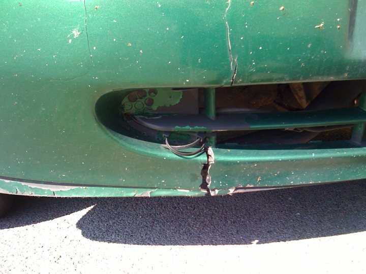 Rust Advice Ford KA - Page 1 - General Gassing - PistonHeads - This is a close-up photograph of a vehicle, possibly from a car, focusing particularly on its lower front area. The green fender is prominently visible, showing signs of wear and possibly some damage, although not substantial. There are some black spots or smudges on the surface, which might be dirt, dirt, or black sand or sandy material on the ground near the fender.