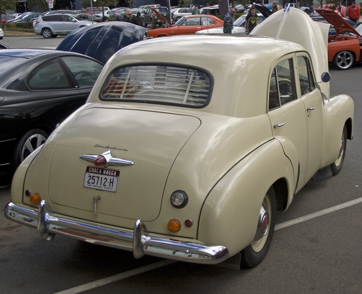 Classics left to die/rotting pics - Vol 2 - Page 214 - Classic Cars and Yesterday's Heroes - PistonHeads - The image shows an older model car parked in a lot. The car is a beige or light tan color, and it has chrome bumpers. On the back of the car, there is a license plate that reads "CHA 251". The vehicle has a vintage aesthetic and appears to be a part of an event or gathering, as there are many other cars in the background, some with their hoods open as if being prepared for a competition or display. The ground surface in the photo is paved, and the sky overhead is blue.