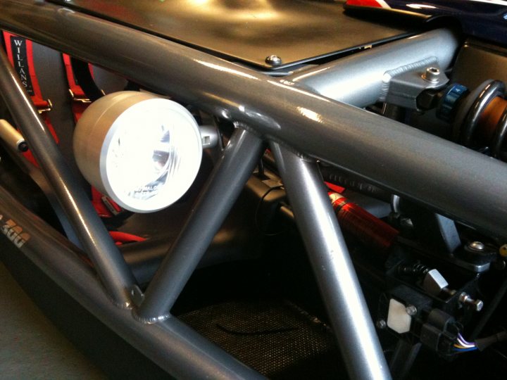 Pistonheads Led Atom Lights - The image showcases an interior view of a vehicle's cargo area. A prominently positioned searchlight is located in front of the grey metallic poles that architect the interior space. This searchlight, with its distinct cylindrical shape and metallic finish, actively shines, casting light on the black carpeted floor. The handle to the lid of the cargo area is also visible, indicating a welcoming entry or exit to this section of the vehicle. The vehicle itself is large and has a red and black striped theme running along its side, adding a vibrant touch to the overall muted color palette.