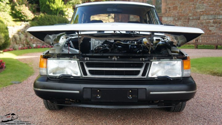 Classic Saab 900 26000 Miles - Page 1 - Saab - PistonHeads - The image shows the front of a dark-colored pickup truck parked on a gravel driveway. The hood of the vehicle is open, revealing the engine compartment. The truck appears to be a full-crew model, suggesting it has four doors and is likely intended for off-road use. The gravel driveway has red brick edging, and there is a neat lawn and garden area in the background, indicating a domestic setting. The trees behind the truck suggest it may be in a suburban or rural area during the daytime.