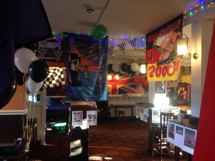 BBQ at 2:30 am - Just keeps on rolling - Page 121 - HSV & Monaro - PistonHeads - The image depicts an interior of what appears to be a themed party room. The room is decorated with various items, including a prominent racing car motif. Multiple flags with the checkered pattern of the British Union Jack hang prominently on the walls, suggesting a tie to motorsport, possibly rally racing. Numerous black and white checkered balloons are strewn throughout the room, reinforcing the vehicle racing theme. Board games are also scattered around the room, hinting at additional recreational activities in the space. The ceiling is adorned with strands of small, round lights, giving the room a festive and cozy ambiance.